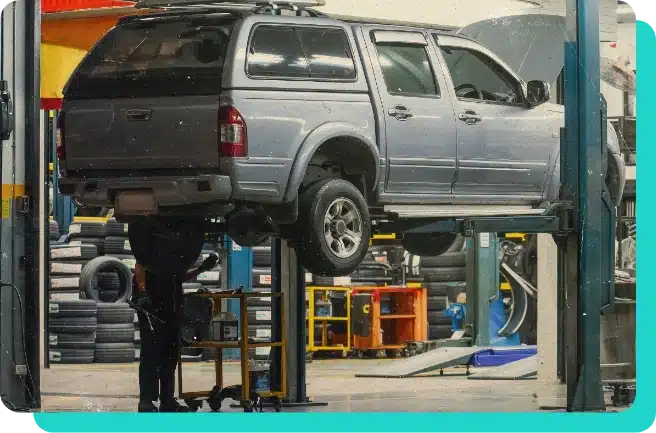 image of a light blue pickup truck with cab cover raised on lift in the shop bay.