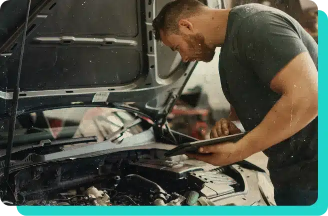 Image of mechanic leaning over car engine while hood is up inspecting the engine for services in the shop.