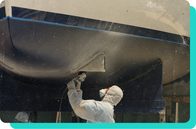 Image of mechanic spraying paint on the bottom of a boat for repairs.