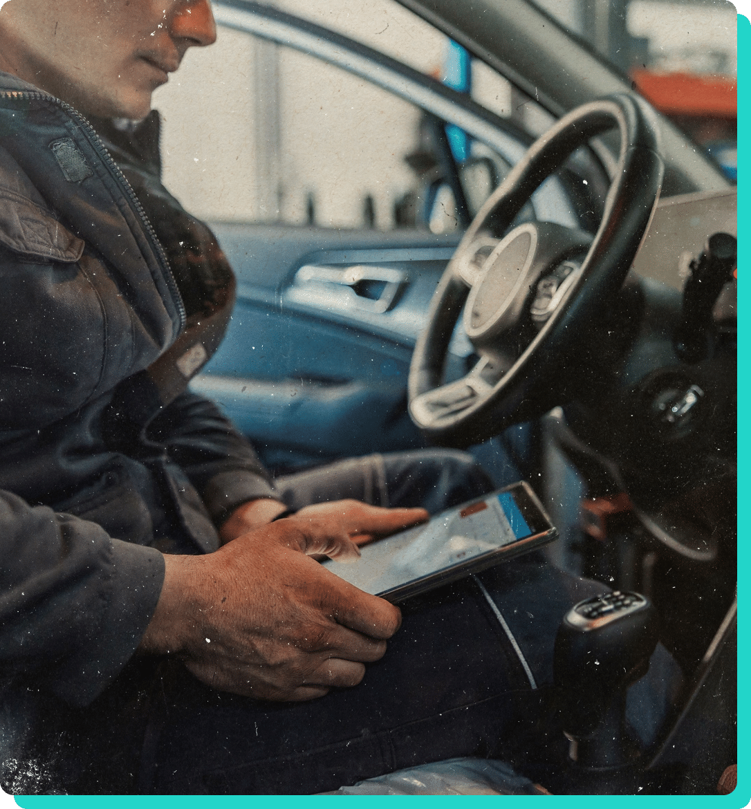 Preventative maintenance for cars and trucks in Wells, VT at Thomas' Auto Repair. Image of male mechanic wearing a brown bomber jacket holding diagnostic tool while sitting in driver seat of a car that is in the shop for services.